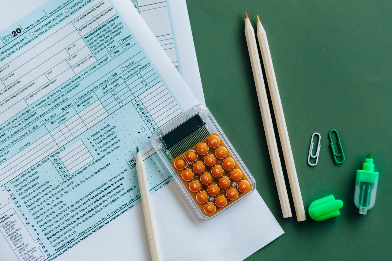 services-01 Flat lay of tax forms, calculator, pencils, and clips on green surface, ideal for finance or accounting themes.