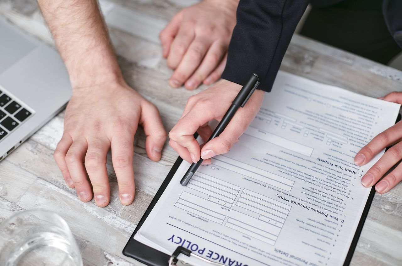 team-02 Close-up image of two people signing an insurance policy document on a wooden desk.